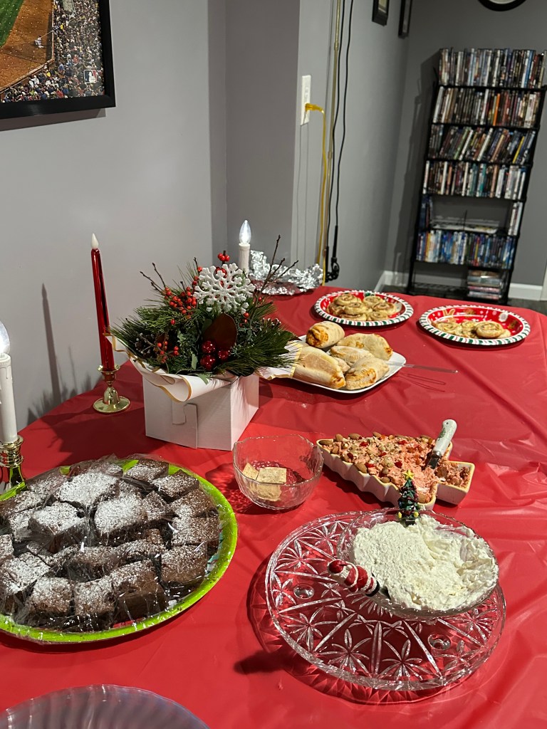 A festive table setting featuring a variety of holiday treats including chocolate brownies, pastries, and a decorated dish with cream. The table is adorned with a holiday centerpiece and candles.